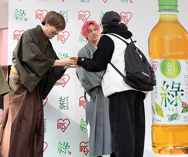 ▲一般客に「アイリスのお茶 綠（りょく）」を手渡しするEXITとエルフ