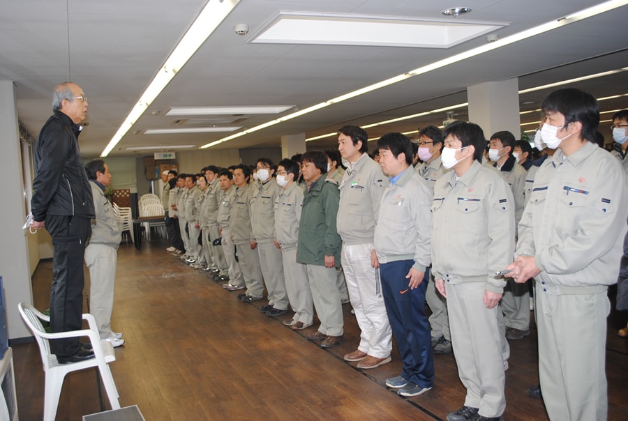 社員を前に想いを伝える健太郎。破れた壁や倒れた家具による粉塵から身を守るため、多くの社員がマスクを着用している。